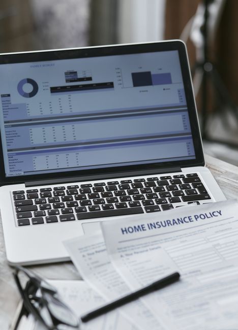 The image depicts a workspace with a laptop displaying various charts and data graphs related to gardening and landscaping work, situated on a wooden surface. In front of the laptop, there are documen